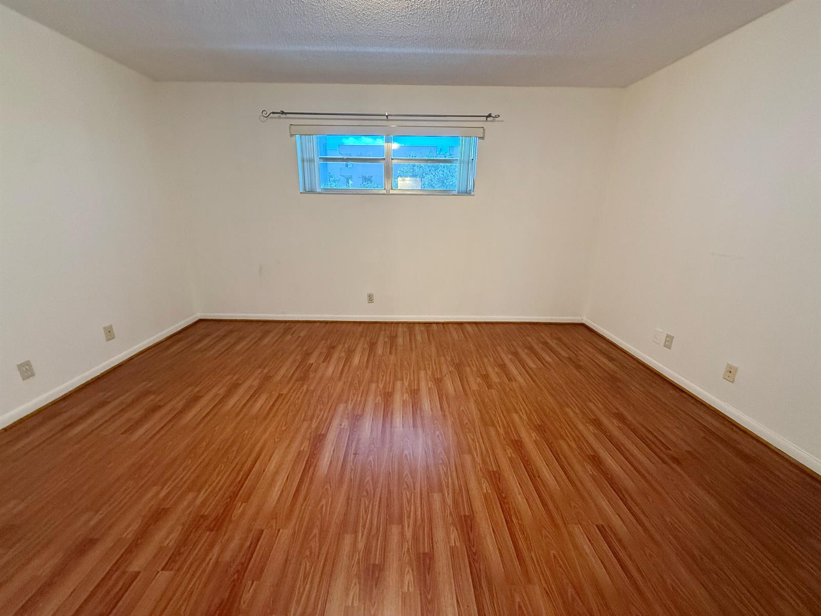 An empty room with white walls, wood-look laminate flooring, and a single window — 3776 Inverrary Boulevard # 204r, Lauderhill FL 33319, LAUDERHILL, FL