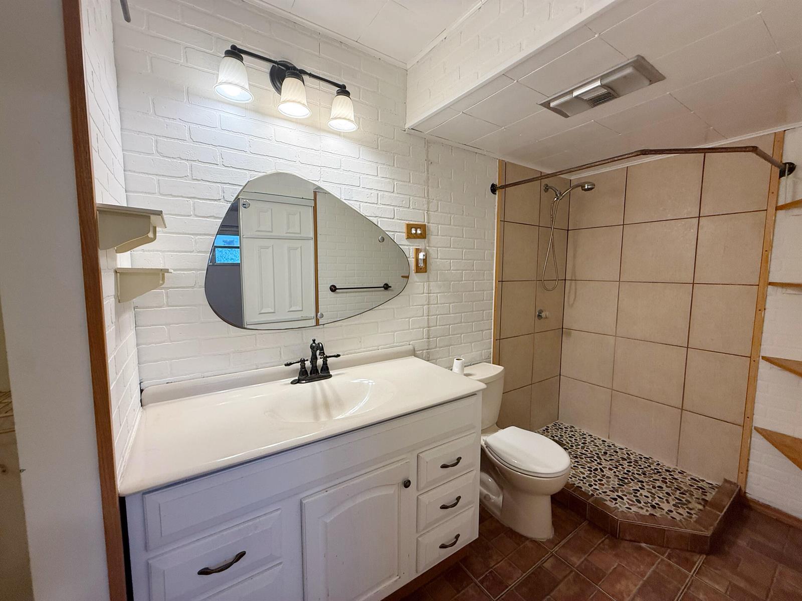 A bathroom features a white vanity, an irregular mirror, a brick wall, and a tiled shower — 3776 Inverrary Boulevard # 204r, Lauderhill FL 33319, LAUDERHILL, FL