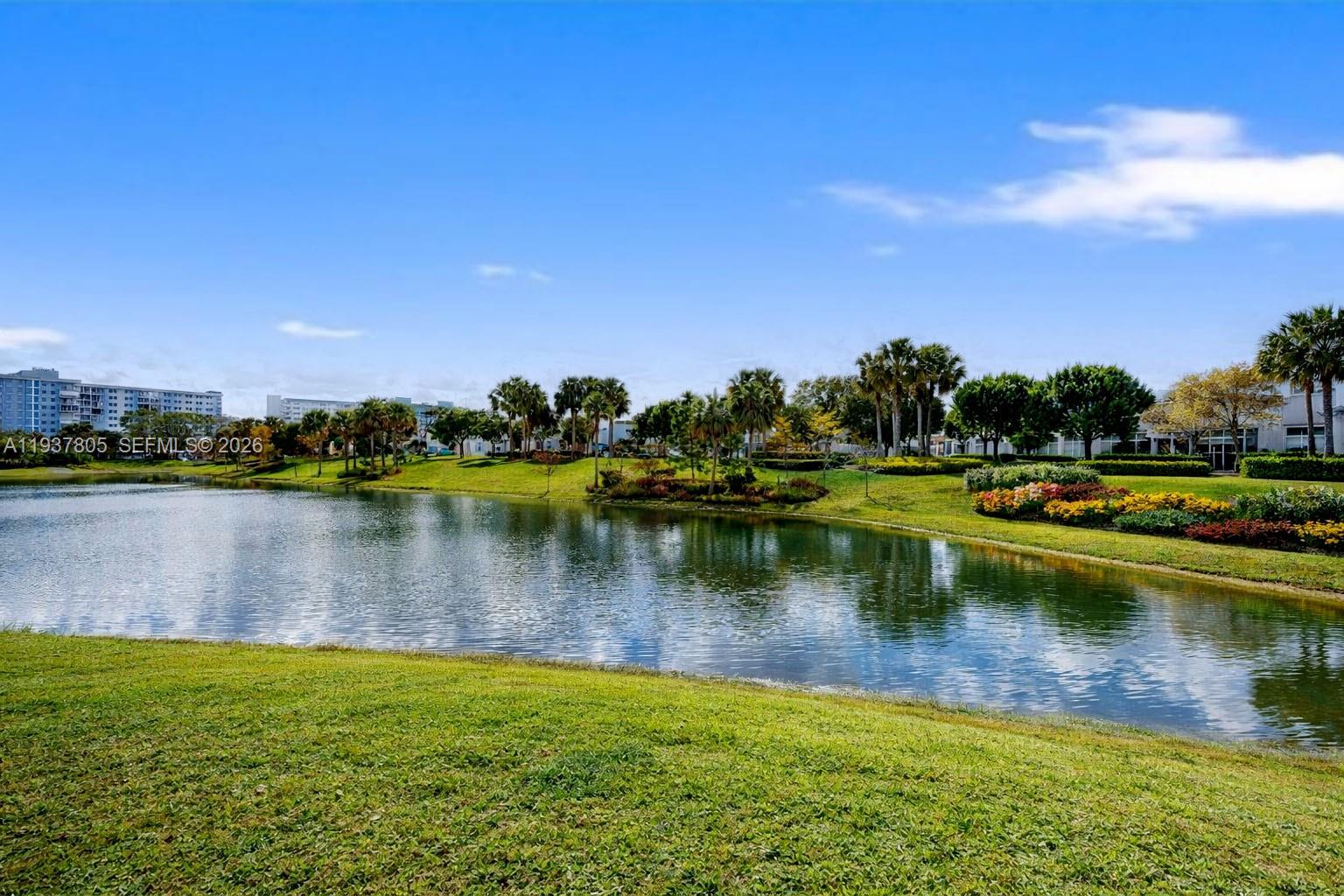 A calm pond sits in front of a landscaped lawn with trees and distant buildings — 3850 Washington St # 314, Hollywood FL 33021, HOLLYWOOD, FL
