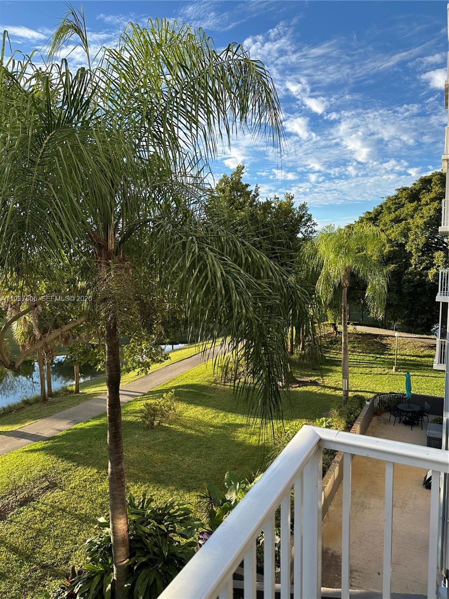 A view from a balcony overlooking a grassy lawn, palm trees, and a small pond — 3850 Washington St # 314, Hollywood FL 33021, HOLLYWOOD, FL