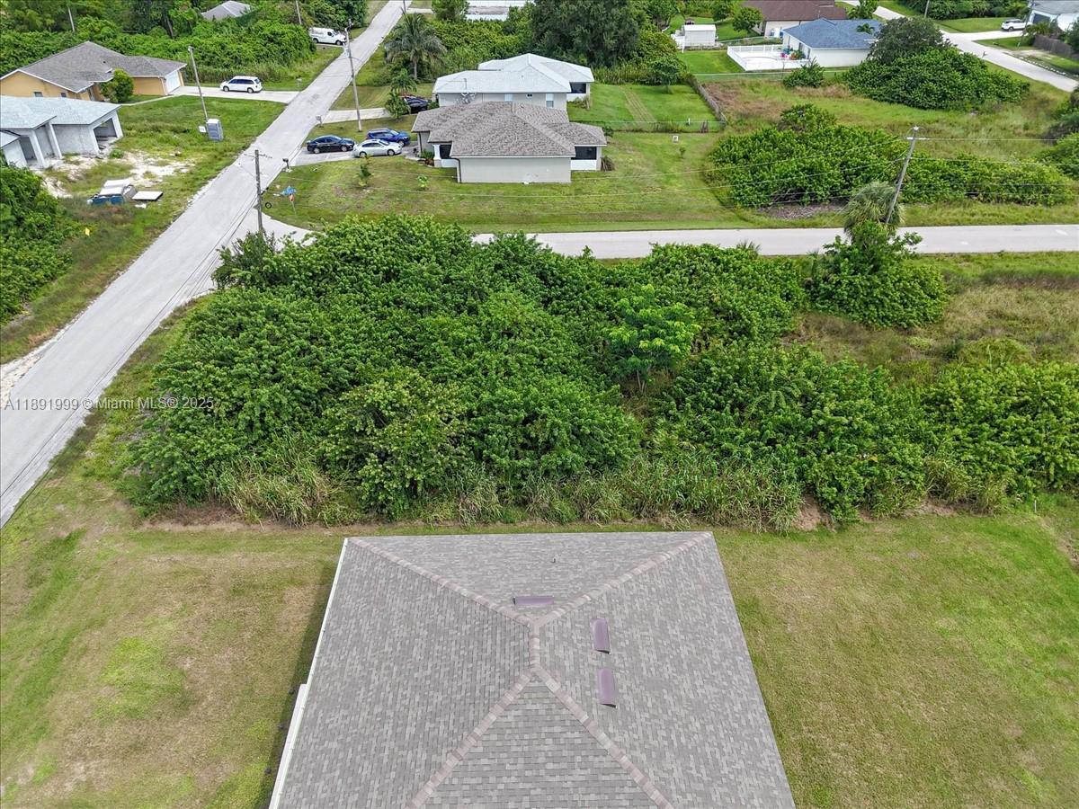 An aerial view shows a house roof overlooking a large, densely wooded vacant lot — 4201 15 ST SW, Lehigh Acres FL 33976, LEHIGH ACRES, FL