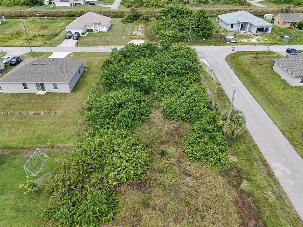 An aerial view shows a vacant, overgrown residential lot situated between two houses — 4201 15 ST SW, Lehigh Acres FL 33976, LEHIGH ACRES, FL