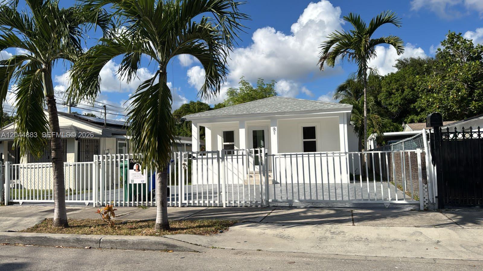 A white, single-story house with a front porch sits behind a metal fence and palms — 81 NW 44th St, Miami FL 33127, MIAMI, FL
