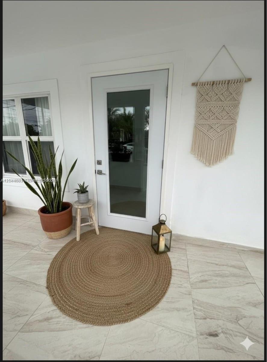A white front door with a glass panel sits on a tiled porch with decor — 81 NW 44th St, Miami FL 33127, MIAMI, FL