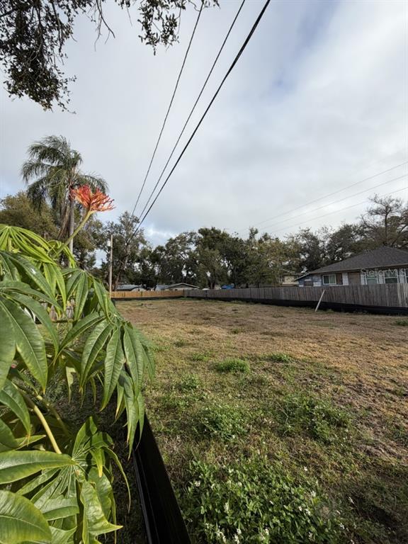 A vacant, grassy residential lot is enclosed by a wooden fence under a cloudy sky — 1006 JONES STREET, CLEARWATER, FL