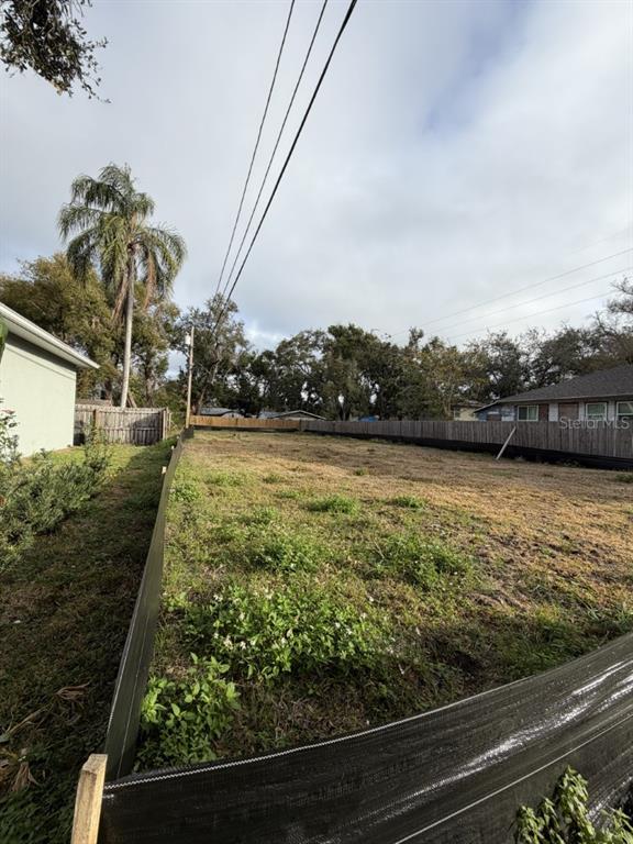 A vacant, fenced-in residential lot features sparse grass and mature trees under a cloudy sky — 1006 JONES STREET, CLEARWATER, FL