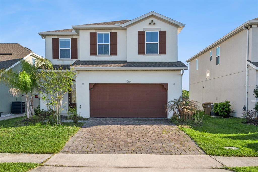 A two-story suburban house with a brown garage door, beige stucco exterior, and paved driveway — 1764 STAMEN DRIVE, KISSIMMEE, FL