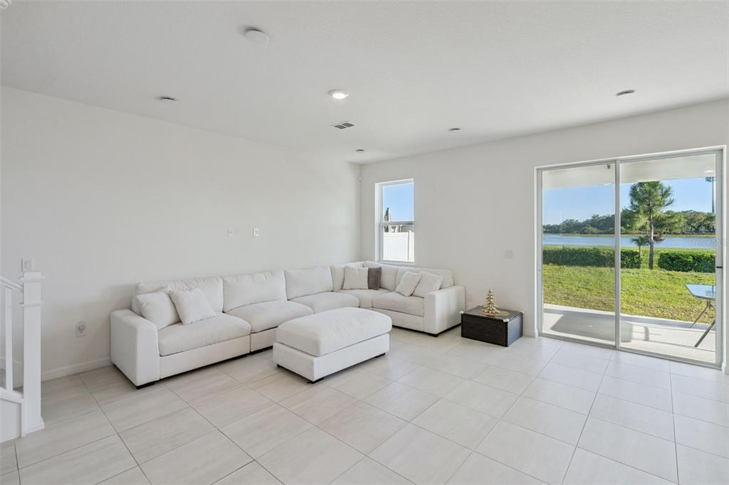 A bright living room features white tile floors, a large sectional sofa, and sliding glass doors — 1764 STAMEN DRIVE, KISSIMMEE, FL