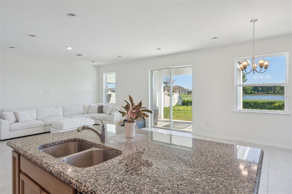 A kitchen island with a granite countertop and double sink overlooks a living area — 1764 STAMEN DRIVE, KISSIMMEE, FL