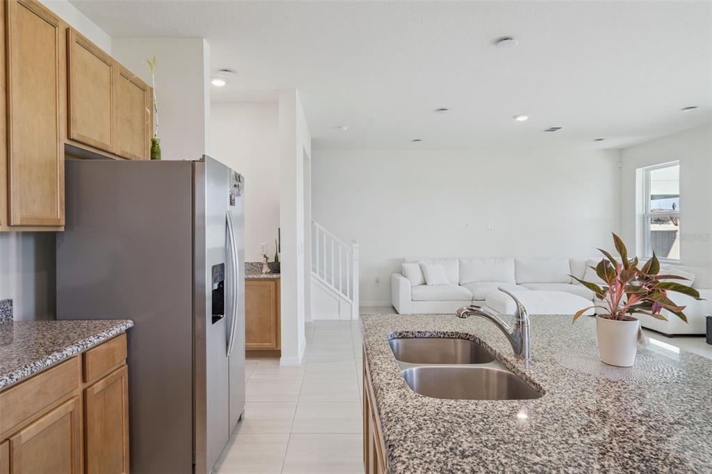 A kitchen with granite countertops and stainless steel appliances overlooks a living room with stairs — 1764 STAMEN DRIVE, KISSIMMEE, FL