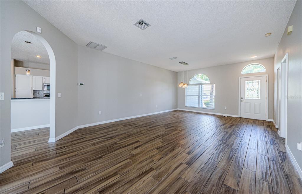 An empty living room features wood-look tile flooring, light gray walls, and an arched entryway — 4801 AUGUSTA AVENUE, OLDSMAR, FL