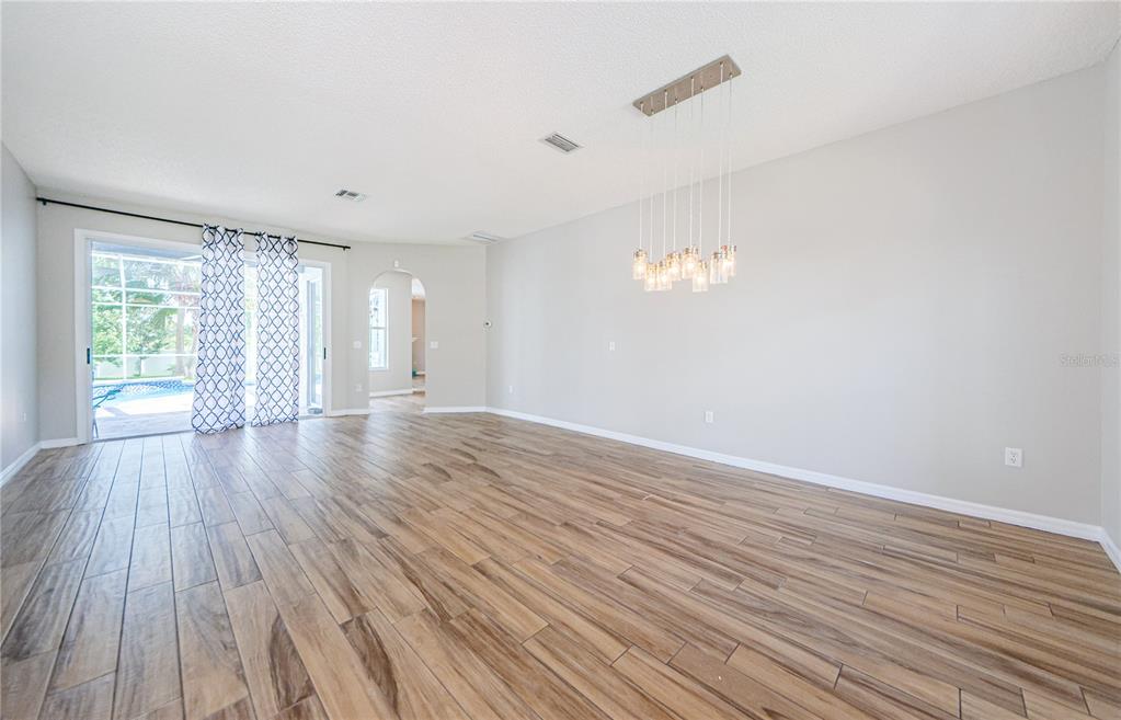A spacious room with wood-look tile flooring, a modern pendant light, and sliding glass doors — 4801 AUGUSTA AVENUE, OLDSMAR, FL