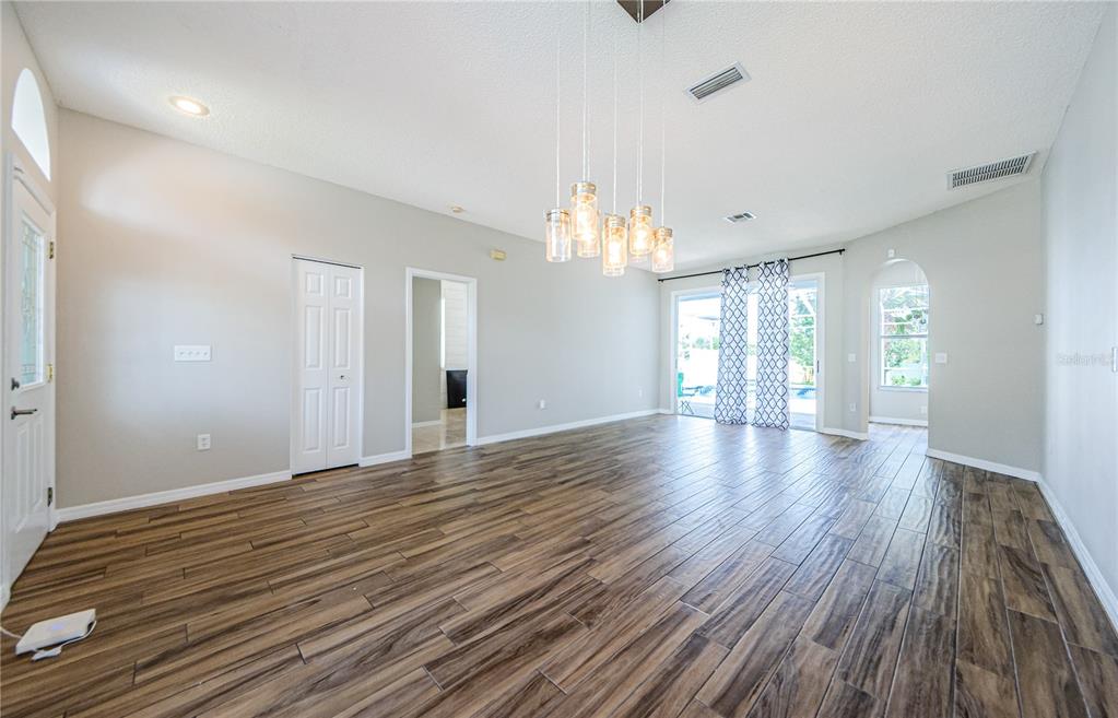 An empty living room features wood-look tile flooring, a vaulted ceiling, and a glass pendant chandelier — 4801 AUGUSTA AVENUE, OLDSMAR, FL