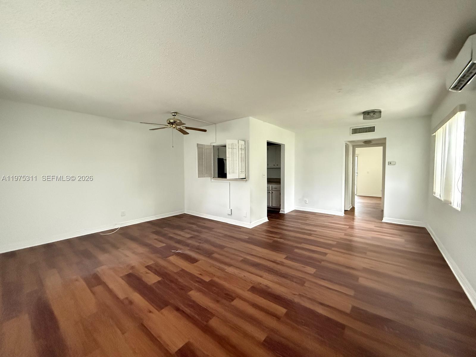 An empty living room features dark wood-look flooring, white walls, a ceiling fan, and shutters — 104 E Easthampton  E # 1, West Palm Beach FL 33417, WEST PALM BEACH, FL