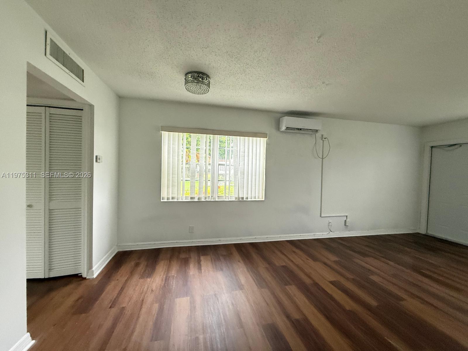 An empty room features wood-look flooring, a window with vertical blinds, and a wall-mounted air conditioner — 104 E Easthampton  E # 1, West Palm Beach FL 33417, WEST PALM BEACH, FL
