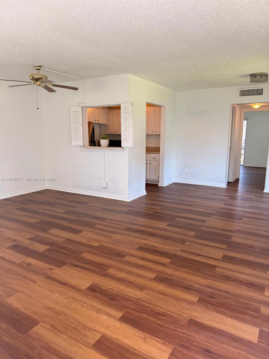 An empty living room features wood-look flooring, a ceiling fan, and a kitchen pass-through window — 104 E Easthampton  E # 1, West Palm Beach FL 33417, WEST PALM BEACH, FL