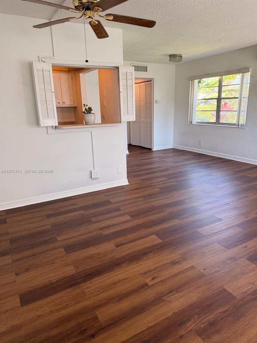 This living room features wood-look flooring, a ceiling fan, and a pass-through kitchen window — 104 E Easthampton  E # 1, West Palm Beach FL 33417, WEST PALM BEACH, FL
