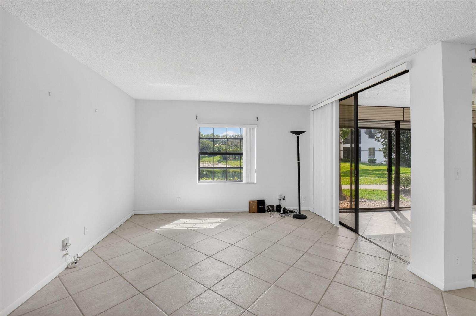 An empty living room with light tile flooring, a window overlooking a pond, and sliding doors — 5415 Verona Drive # F, Boynton Beach FL 33437, BOYNTON BEACH, FL