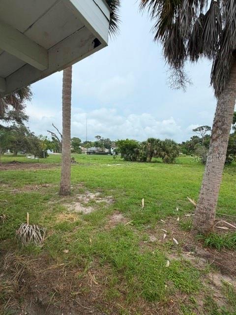 A view of a grassy, undeveloped lot framed by palm trees and a building overhang — 1604 BAYSHORE ROAD, NOKOMIS, FL