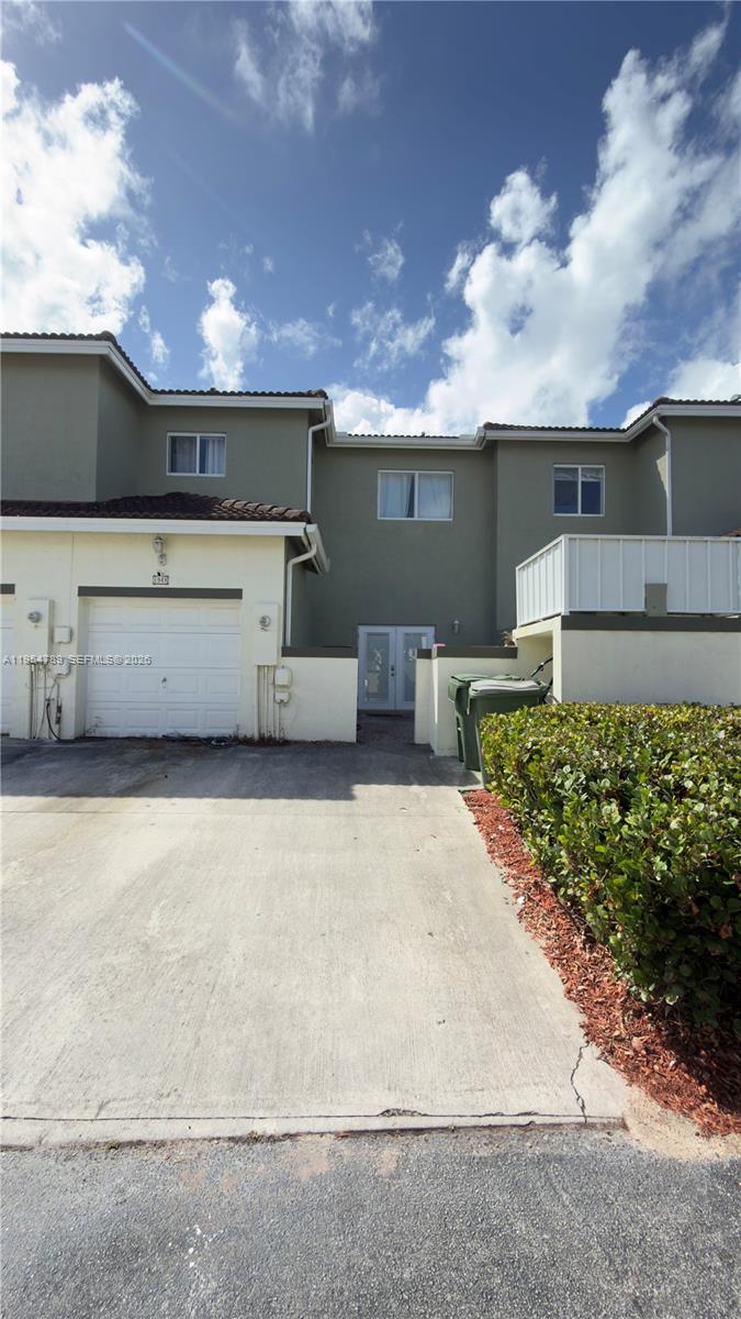 A two-story townhouse exterior features a white garage, a concrete driveway, and a small courtyard — 1948 SE 24th Ave, Homestead FL 33035, HOMESTEAD, FL