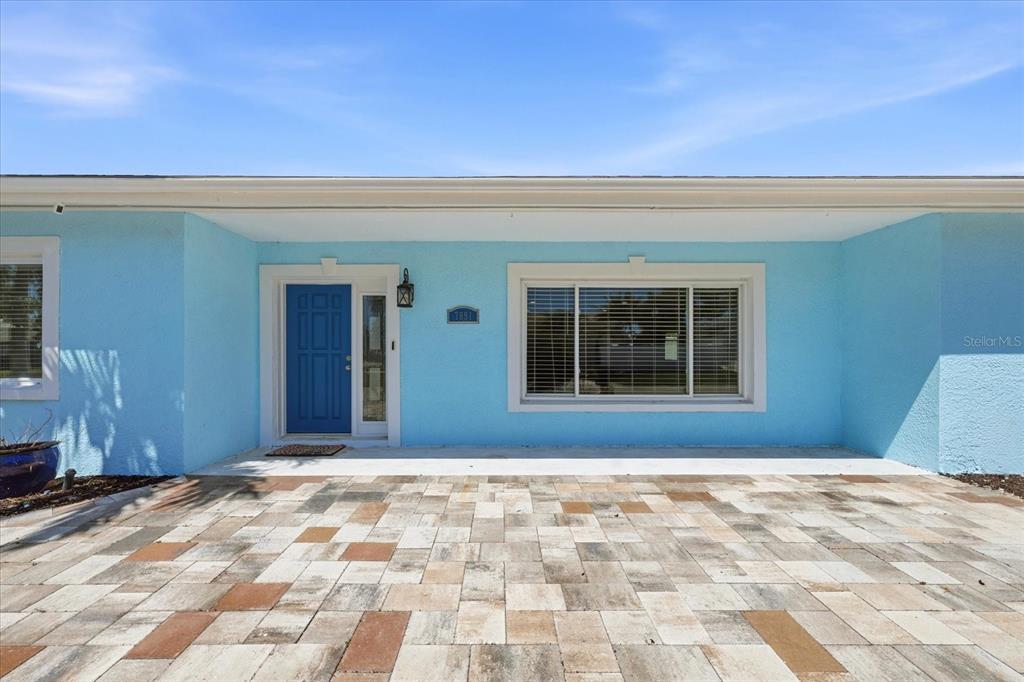The exterior of a light blue house features a blue front door and paver patio — 7891 4TH AVENUE S, ST PETERSBURG, FL