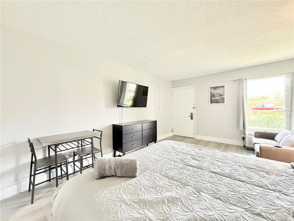 A bedroom features a bed, a black dresser with a wall-mounted television, and a small table — 7150 N TAMIAMI TRAIL UNIT C126, SARASOTA, FL