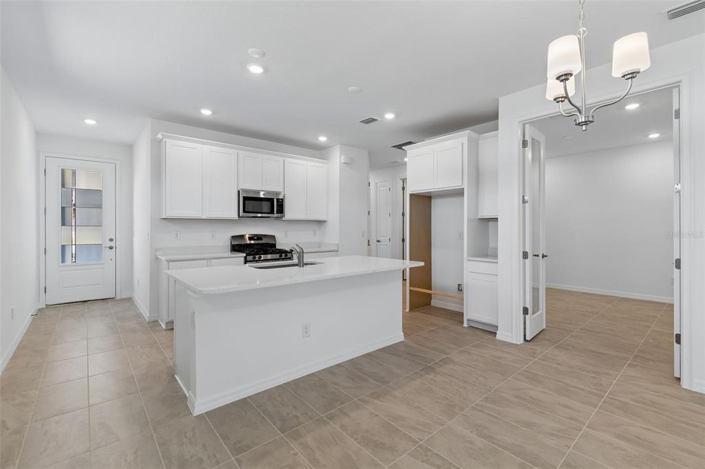 A modern kitchen features white cabinetry, a central island, and tile flooring — 3744 NANDINA CIRCLE, SUN CITY CENTER, FL