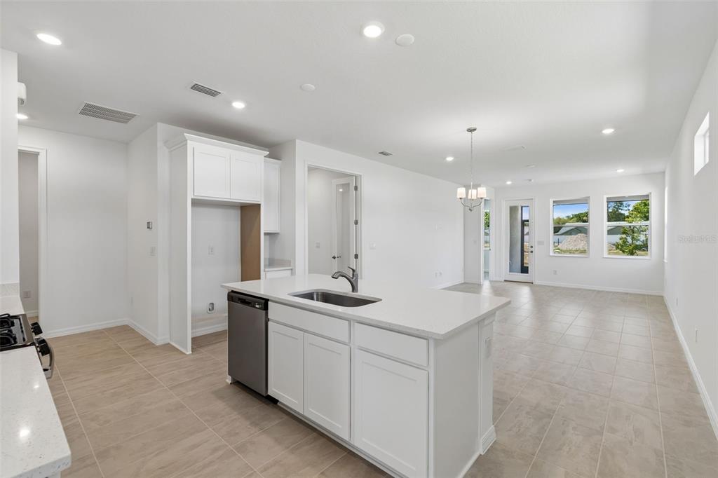 A bright kitchen features a white island with a sink, stainless dishwasher, and tile flooring — 3744 NANDINA CIRCLE, SUN CITY CENTER, FL