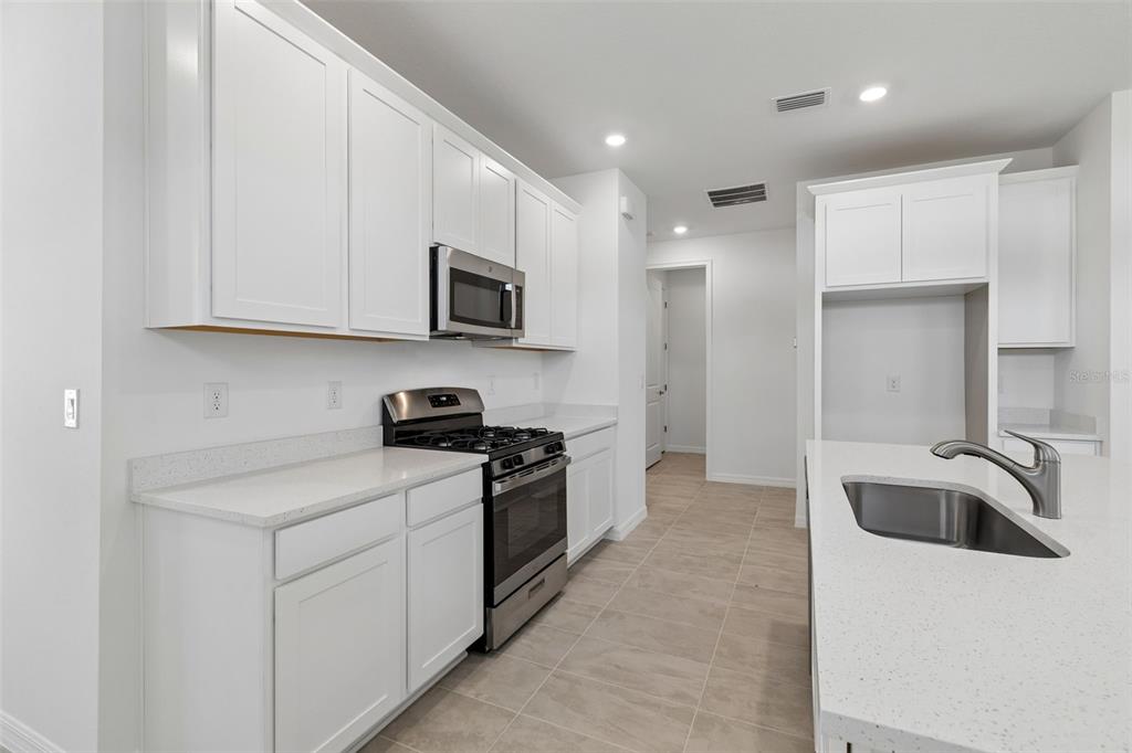 A modern kitchen features white cabinets, stainless steel appliances, and a quartz-topped island — 3744 NANDINA CIRCLE, SUN CITY CENTER, FL