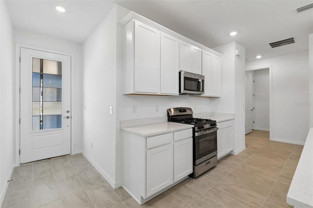 A kitchen features white cabinets, stainless steel appliances, and light-colored tile flooring — 3744 NANDINA CIRCLE, SUN CITY CENTER, FL