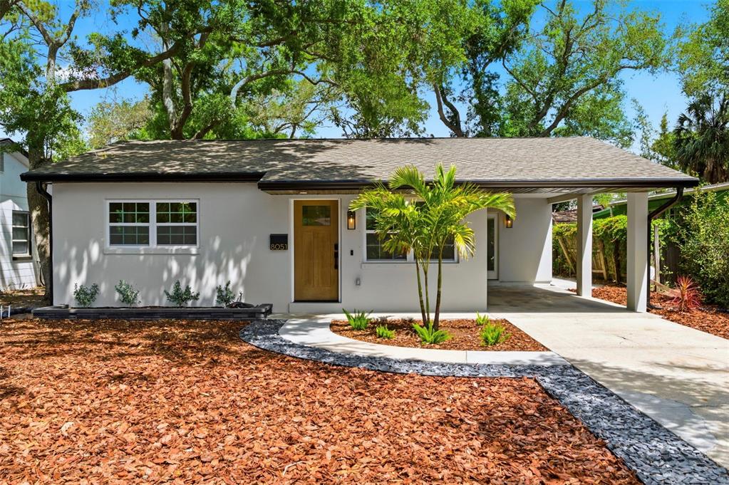 A single-story house with a light-colored exterior, a wooden front door, and a carport — 8051 26TH AVENUE N, ST PETERSBURG, FL
