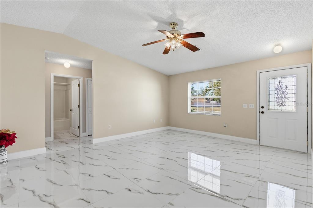 A bright room features white marble-look tile flooring, beige walls, a ceiling fan, and a door — 4320 BAYRIDGE COURT, SPRING HILL, FL