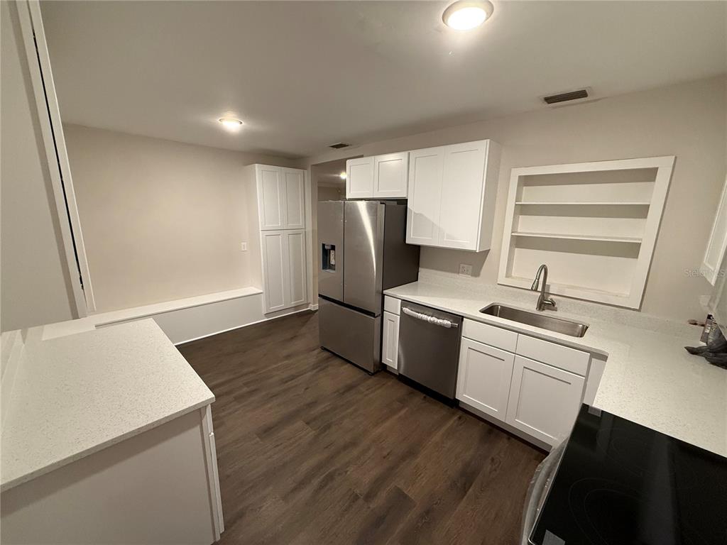 A kitchen features white cabinets, stainless steel appliances, quartz countertops, and dark wood-look flooring — 6215 S KELLY ROAD, TAMPA, FL