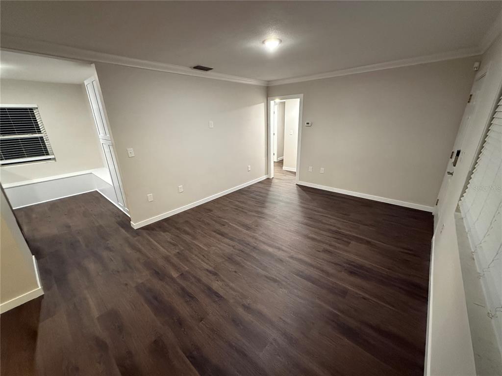 An empty room features dark wood-look flooring, light-colored walls, and a white doorway — 6215 S KELLY ROAD, TAMPA, FL