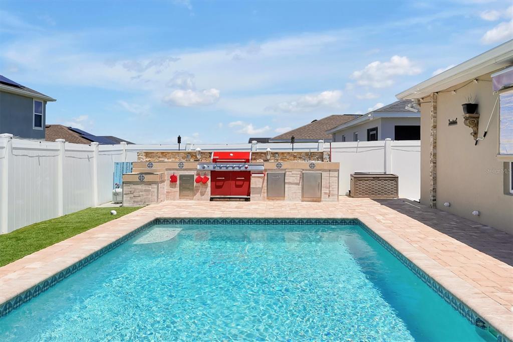 A backyard swimming pool features a stone outdoor kitchen with a red grill — 4055 RUBY RUN, HAINES CITY, FL