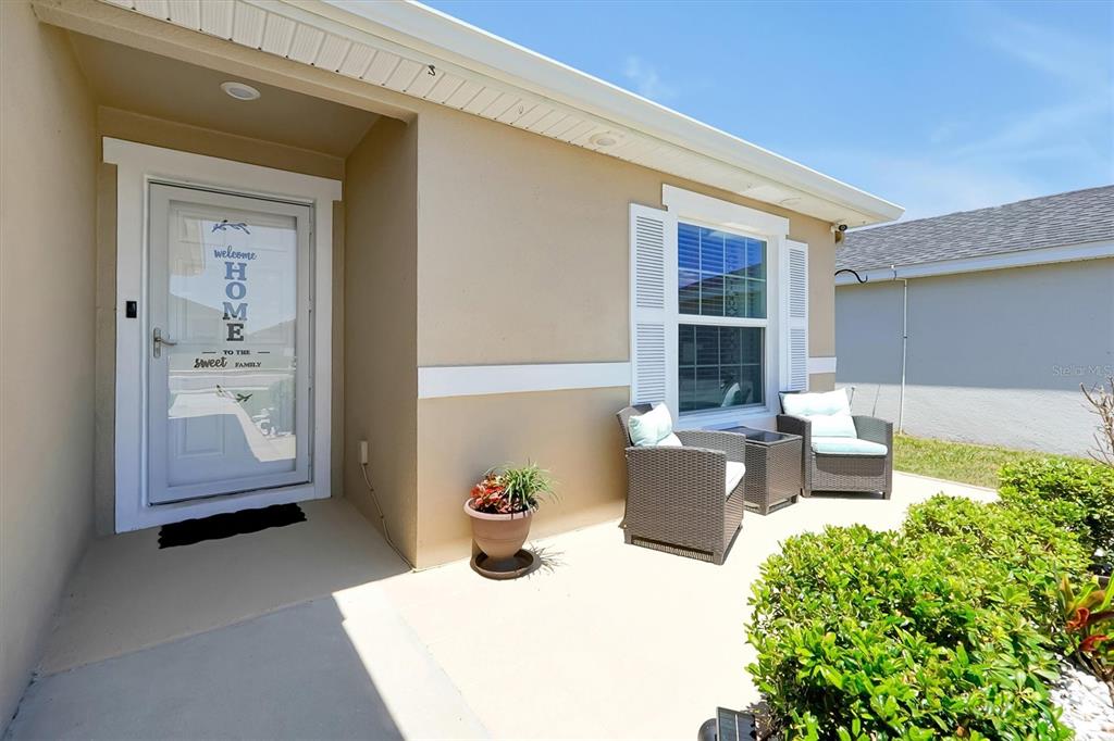 A beige house exterior features a front porch with two chairs and a potted plant — 4055 RUBY RUN, HAINES CITY, FL