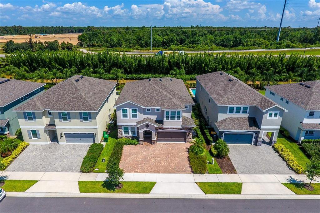 An aerial view shows three suburban houses with paved driveways and green lawns — 7463 MARKER AVENUE, KISSIMMEE, FL