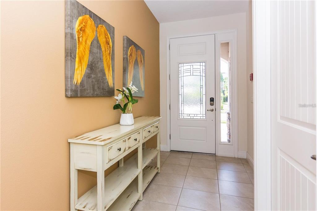 An entryway features a white console table, two angel wing wall canvases, and a glass-paneled door — 7463 MARKER AVENUE, KISSIMMEE, FL