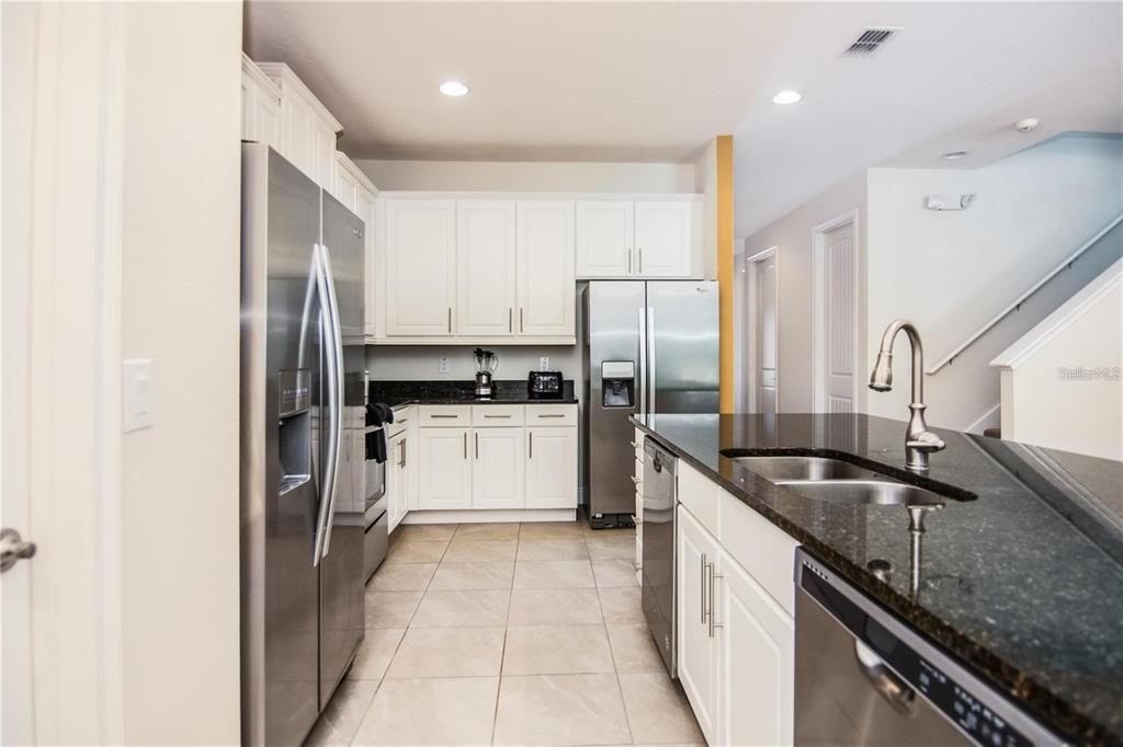 A kitchen with white cabinets, stainless steel appliances, and a dark granite island countertop — 7463 MARKER AVENUE, KISSIMMEE, FL