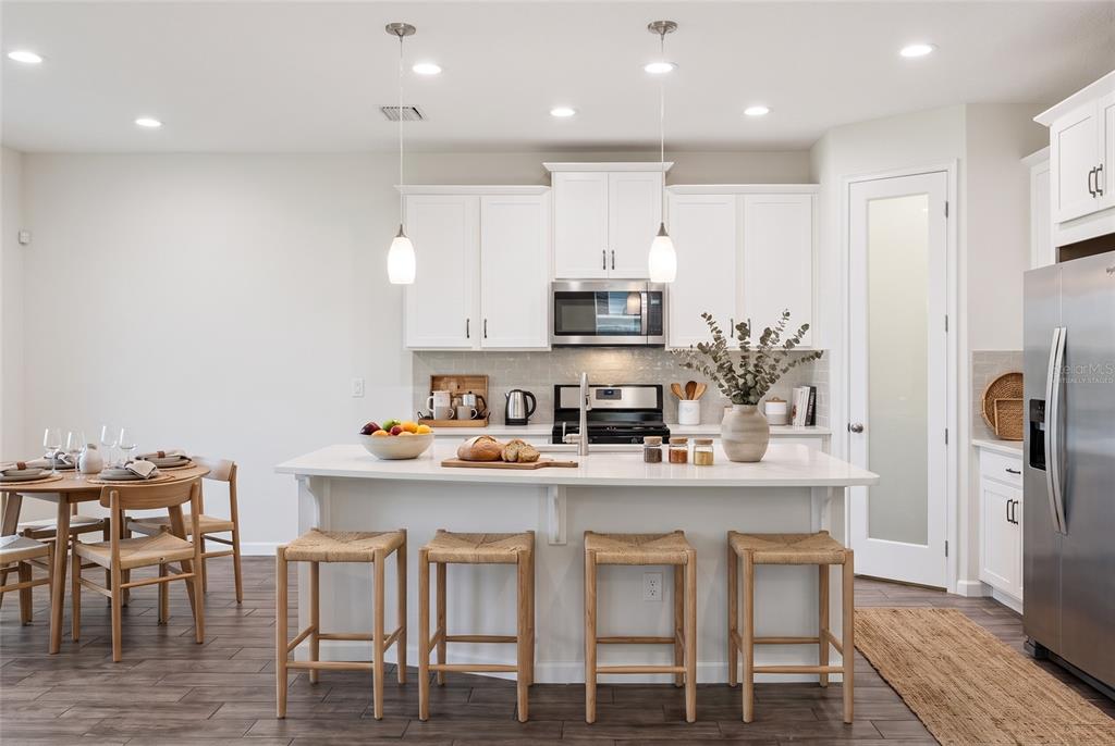 A modern kitchen features white cabinetry, a central island with four stools, and stainless appliances — 8621 RAIN SONG ROAD, SARASOTA, FL