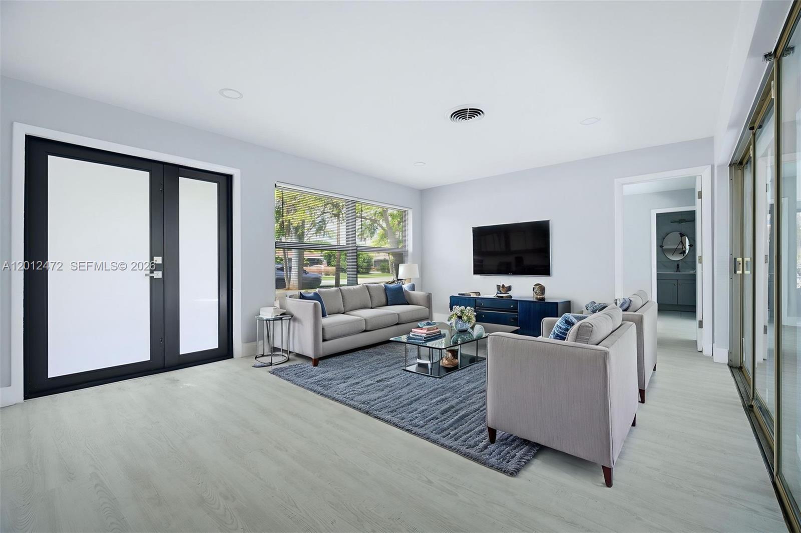 A living room features light wood-look flooring, a grey sofa, and a wall-mounted television — 1930 NW 33rd St, Oakland Park FL 33309, OAKLAND PARK, FL