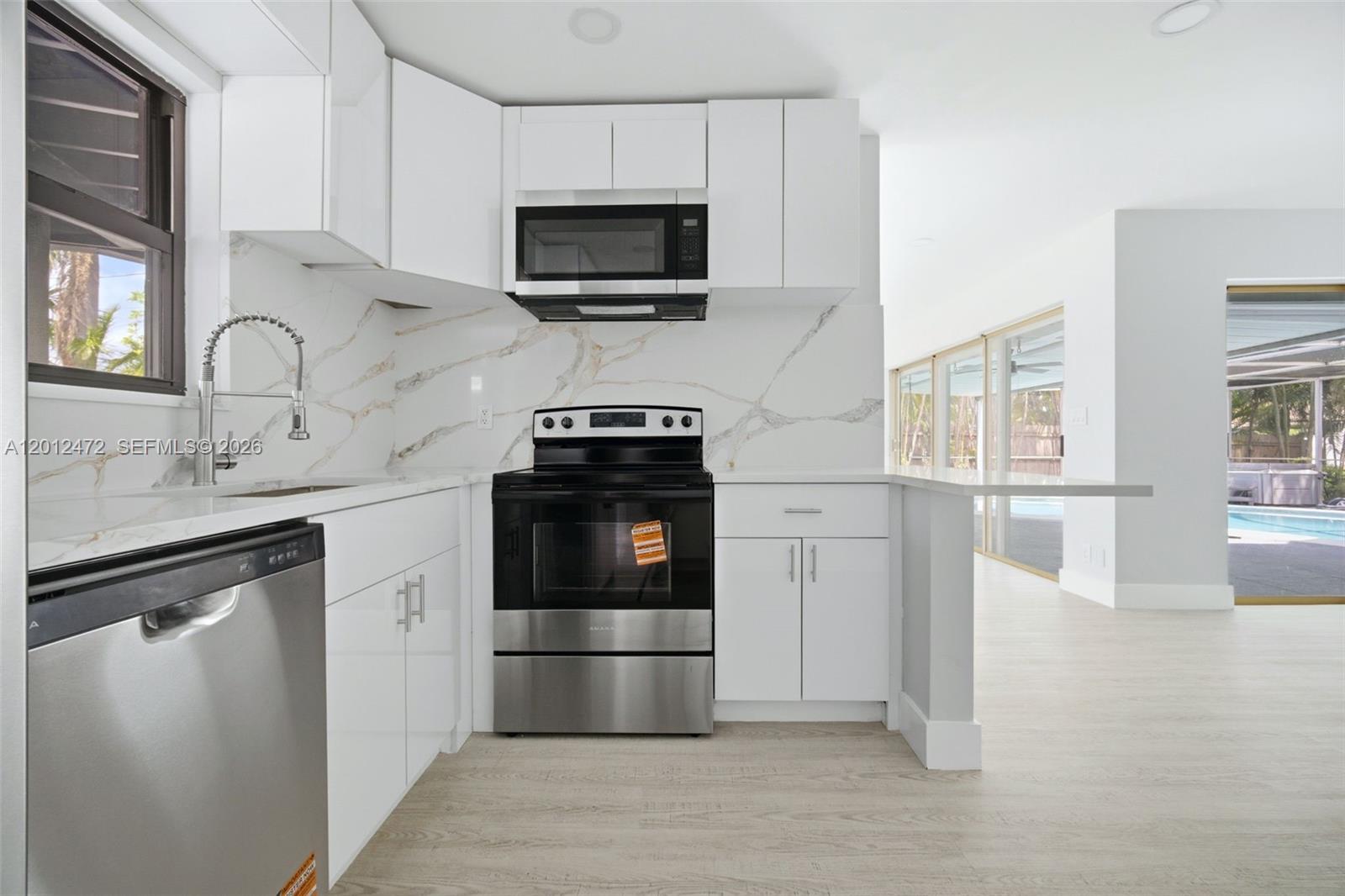 A modern kitchen features white cabinets, stainless steel appliances, and marble-patterned countertops and backsplash — 1930 NW 33rd St, Oakland Park FL 33309, OAKLAND PARK, FL