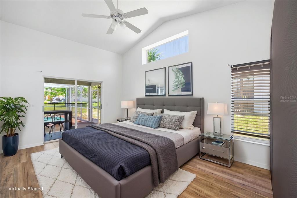 A bedroom with a gray upholstered bed, vaulted ceiling, and sliding doors to a patio — 8316 SUMMERSIDE LANE, PORT RICHEY, FL