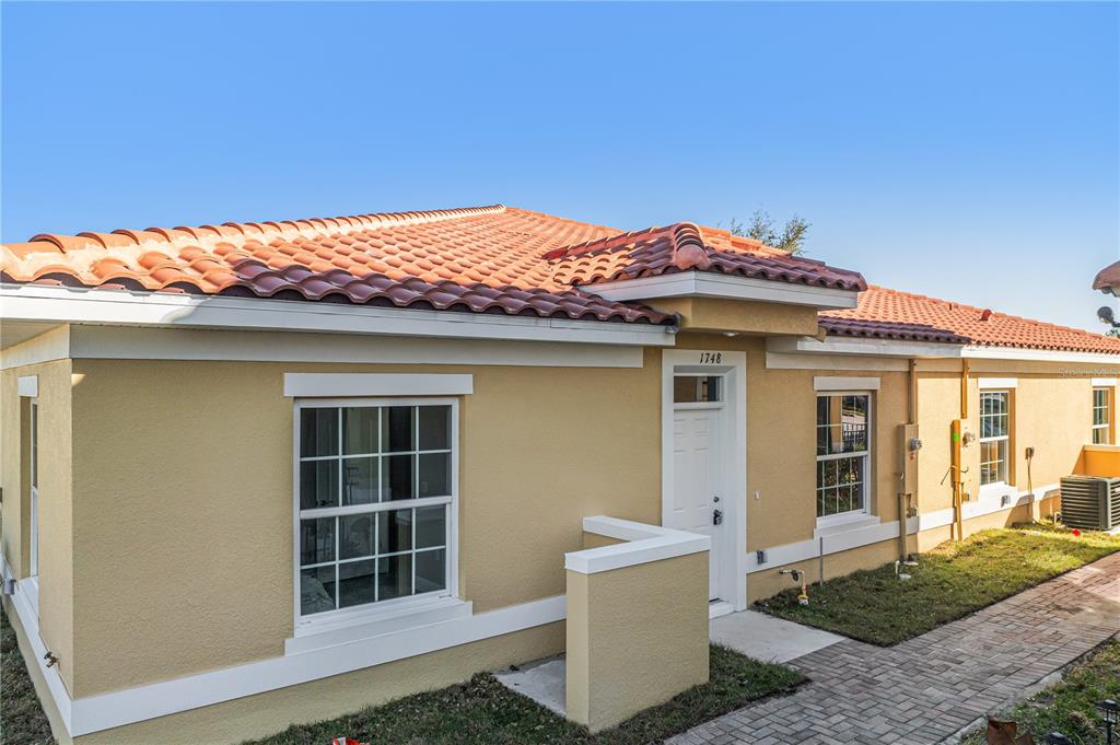 A tan, single-story house with a red tile roof and a brick walkway — 1748 CORIANDER DRIVE, KISSIMMEE, FL