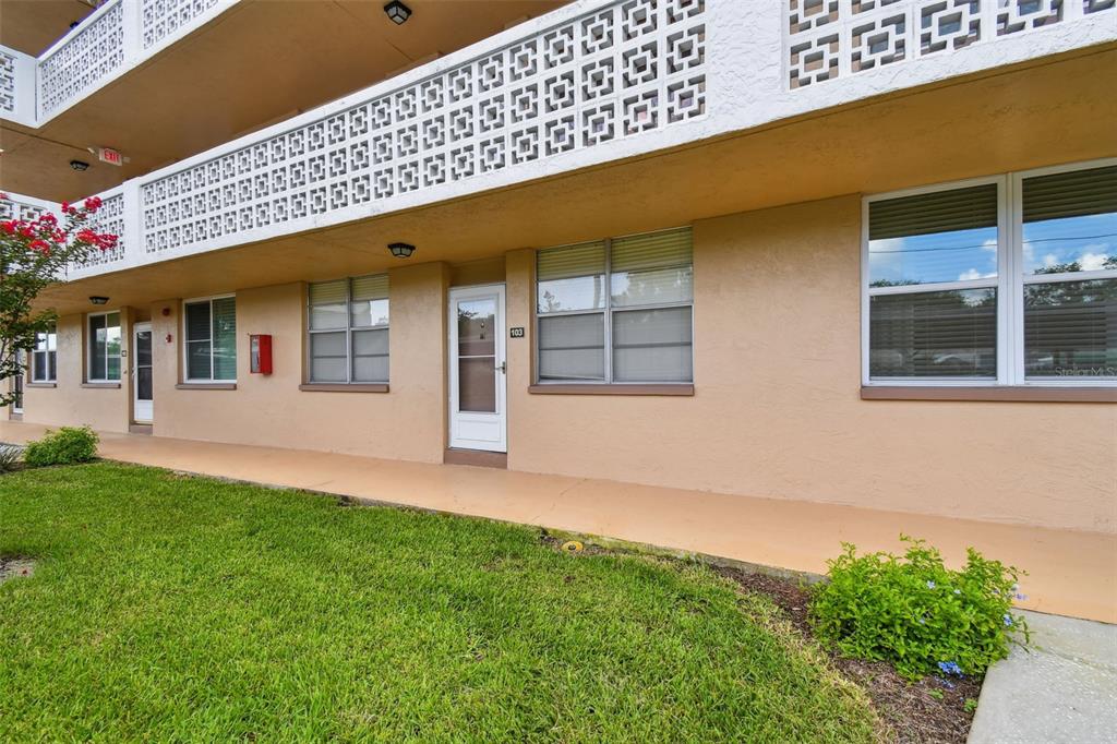 The exterior of a multi-story apartment building features a tan ground-level walkway and unit 103 — 5095 BAY STREET NE UNIT 103, ST PETERSBURG, FL