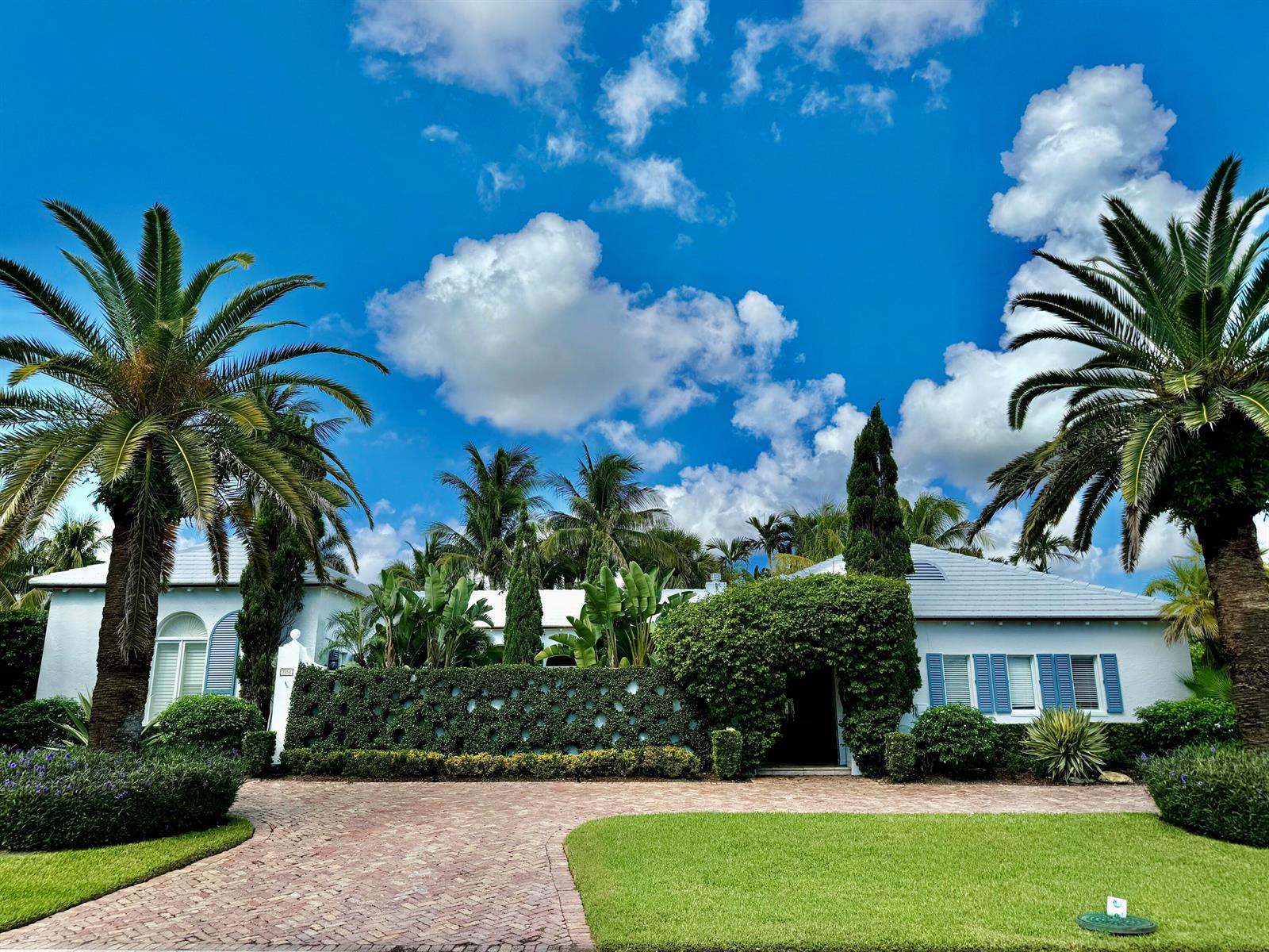 A white house with blue shutters and a brick driveway surrounded by lush palm trees — 2258 E Ibis Isle Rd Road E, Palm Beach FL 33480, PALM BEACH, FL