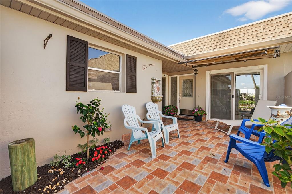 A paved patio features white and blue chairs, a small garden bed, and sliding glass doors — 427 BOCA CIEGA POINT BOULEVARD N, ST PETERSBURG, FL