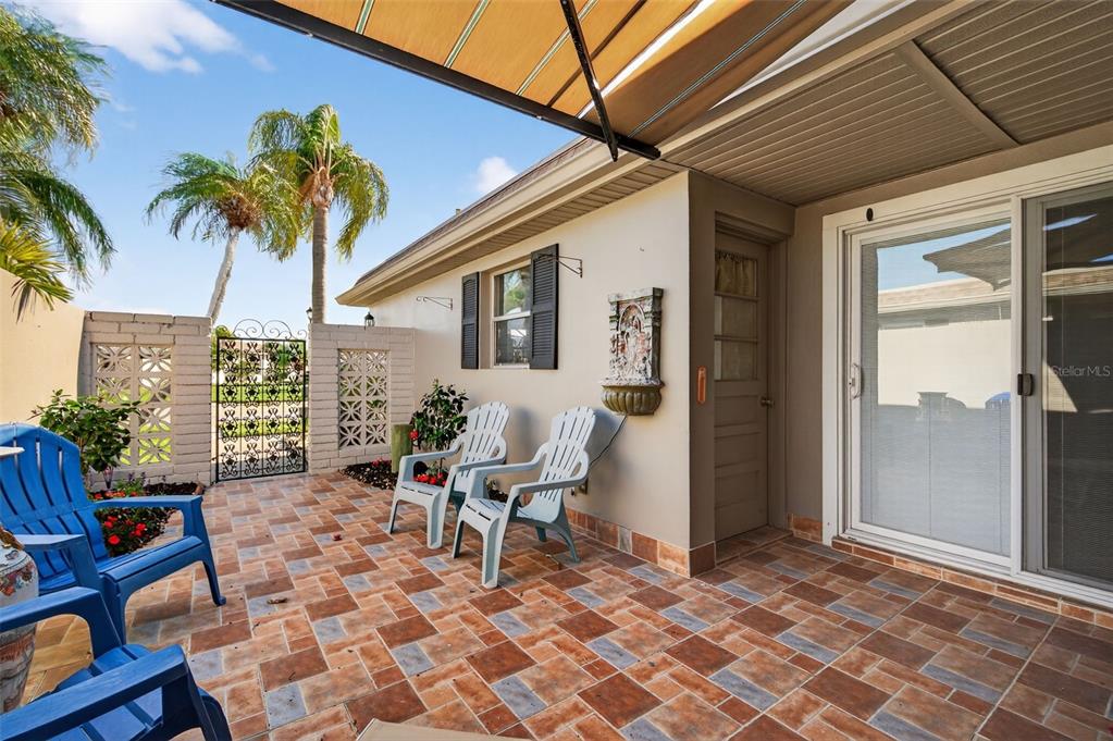A paved patio features white plastic chairs, a decorative wall fountain, and a metal gate — 427 BOCA CIEGA POINT BOULEVARD N, ST PETERSBURG, FL