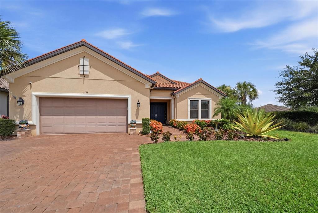 A single-story house with a tan stucco exterior, tile roof, and brick paver driveway — 5288 RUSHMERE COURT, PALMETTO, FL