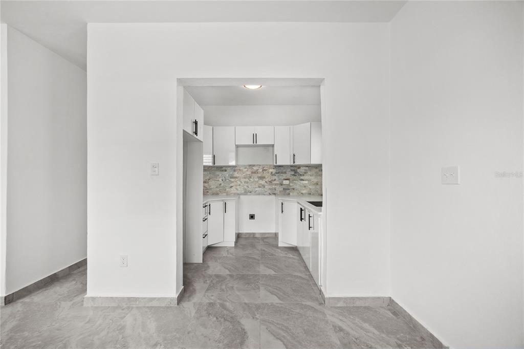 A kitchen with white cabinets, a stone backsplash, and gray tile flooring viewed through an opening — 107 ESPERANZA, LUQUILLO, PR